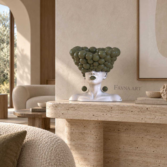 A decorative bust sculpture of a woman with an oversized rounded hairpiece in olive green ral 9003, displayed on a stone console table in a warm, modern living room. The brand name 'FAVNA.