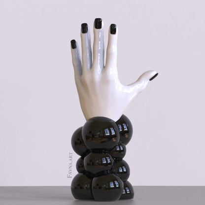 Scultura contemporanea figurativa di design per interni moderni: mano femminile con unghie smaltate e sfere astratte. Scultura artistica moderna in bianco e nero.
